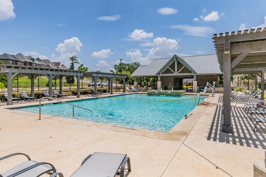 Community swimming pool featuring a concrete deck, multiple timber-frame pergolas, and a covered pavilion with a metal roof and two large propane grilling areas