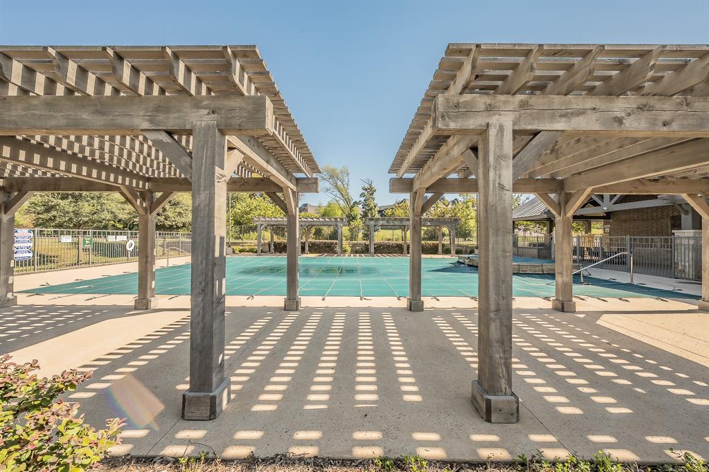 Outdoor community pool area featuring two wooden pergolas, concrete patio decking, and a protective safety cover