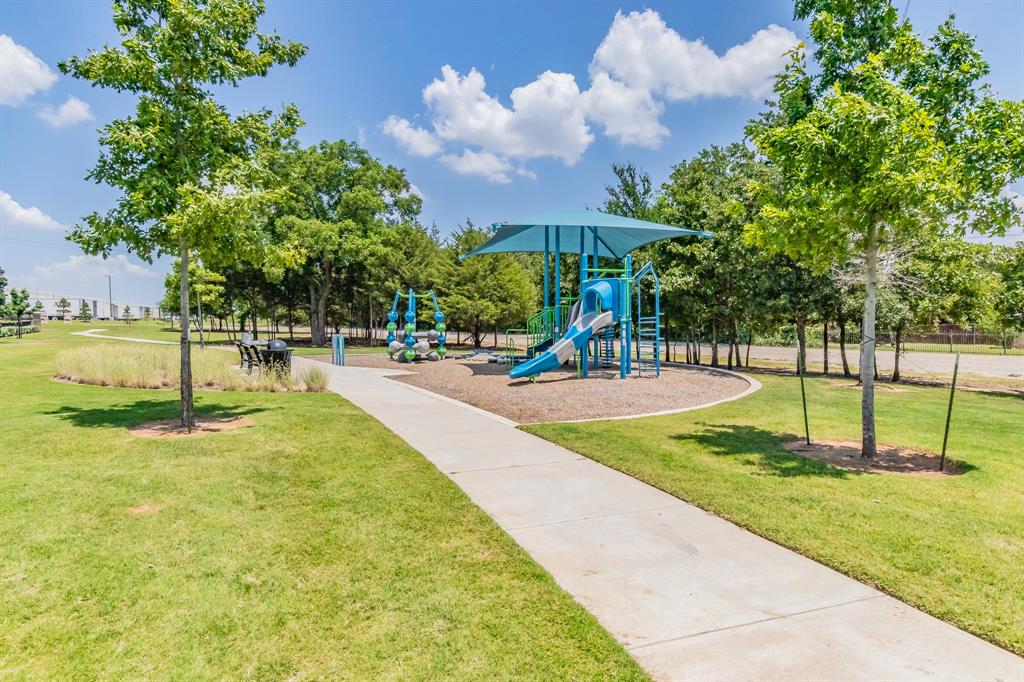 One of two community playground areas featuring a multi-level structure with slide, climbing apparatus, mulch surfacing, and paved pathways near a large greenspace close to property location
