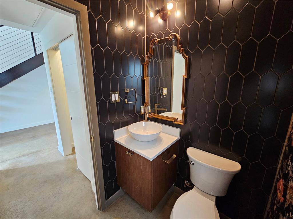 Dark hexagonal wall tiling paired with a wood-finish floating vanity, white stone-surface countertop, white vessel sink, and gold-toned wall-mounted lighting