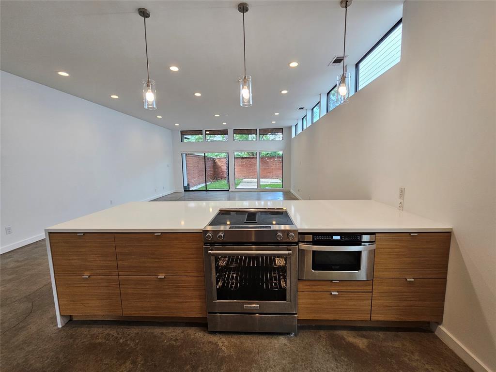Kitchen island featuring wood-finish flat-panel cabinetry, a solid surface countertop, stainless steel slide-in range, built-in microwave, and three glass pendant lights