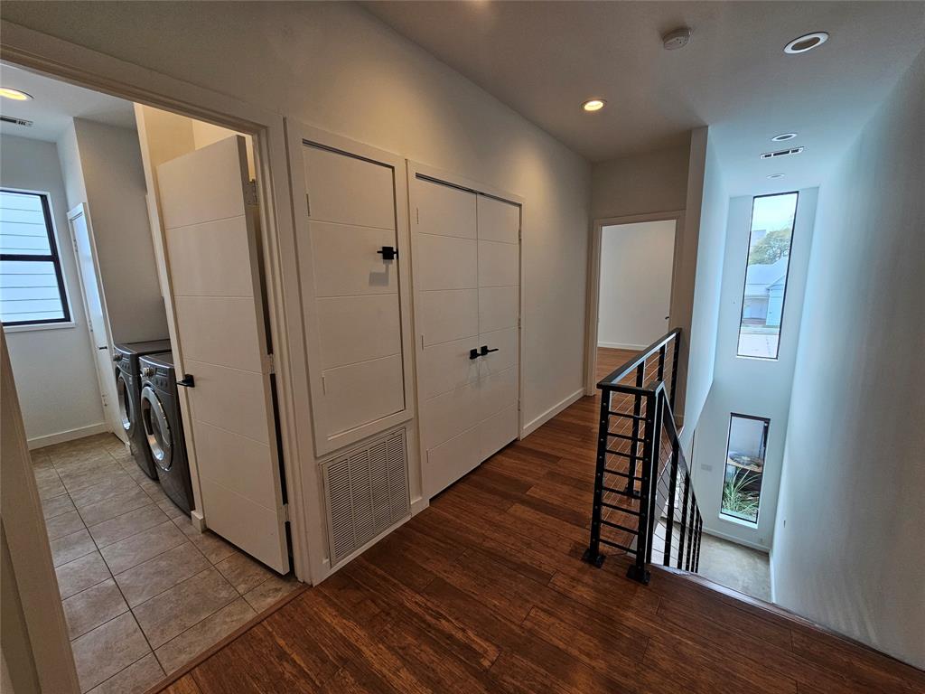 Hallway featuring wood-finish flooring, matte black hardware, recessed lighting, and a metal stair railing with vertical balusters
