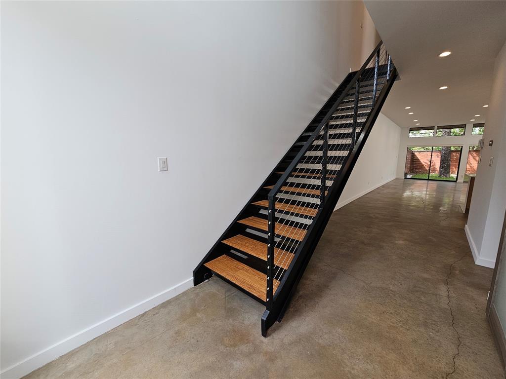 Open-tread staircase with wood-finish planks, black metal stringers, and stainless steel cable railing, complemented by polished concrete flooring and recessed ceiling lighting