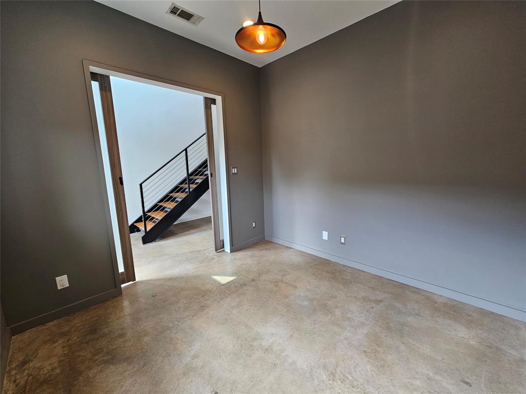 Room with stained concrete flooring, dark-toned walls, and a recessed ceiling light, featuring wood-framed sliding pocket doors opening to a staircase with metal railings