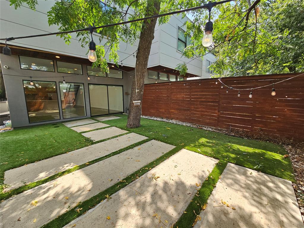 Private rear courtyard featuring large-format concrete pavers, synthetic turf, horizontal wood privacy fencing, and exterior wall-mounted transom windows