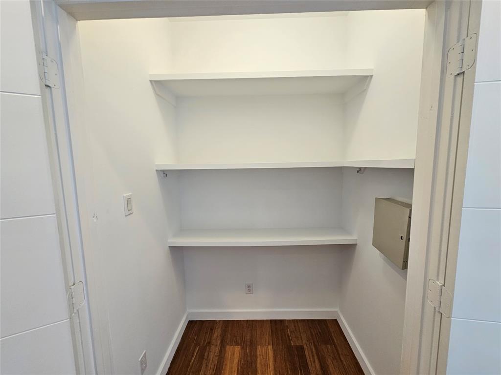 Storage closet featuring wood-finish flooring, three levels of white built-in shelving, and an electrical panel