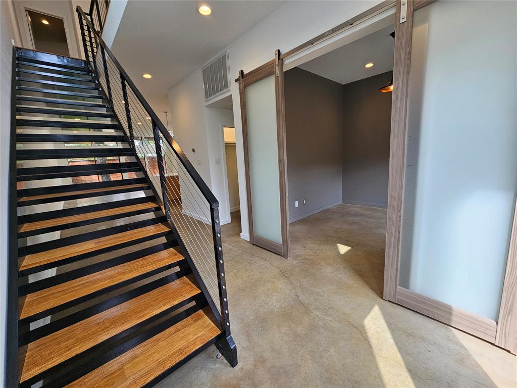 Staircase featuring wood-finish treads and metal railings with cable balusters, paired with a sliding frosted glass barn door and concrete flooring