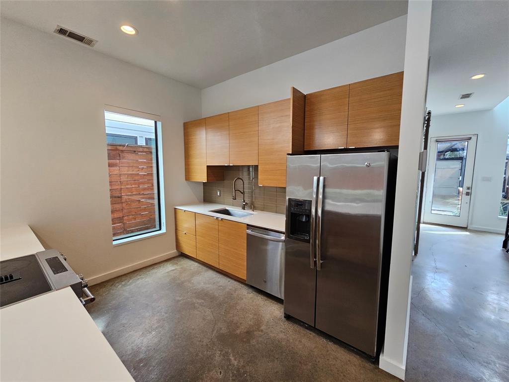 Kitchen featuring flat-panel wood cabinetry, white countertops, stainless steel appliances, and concrete flooring