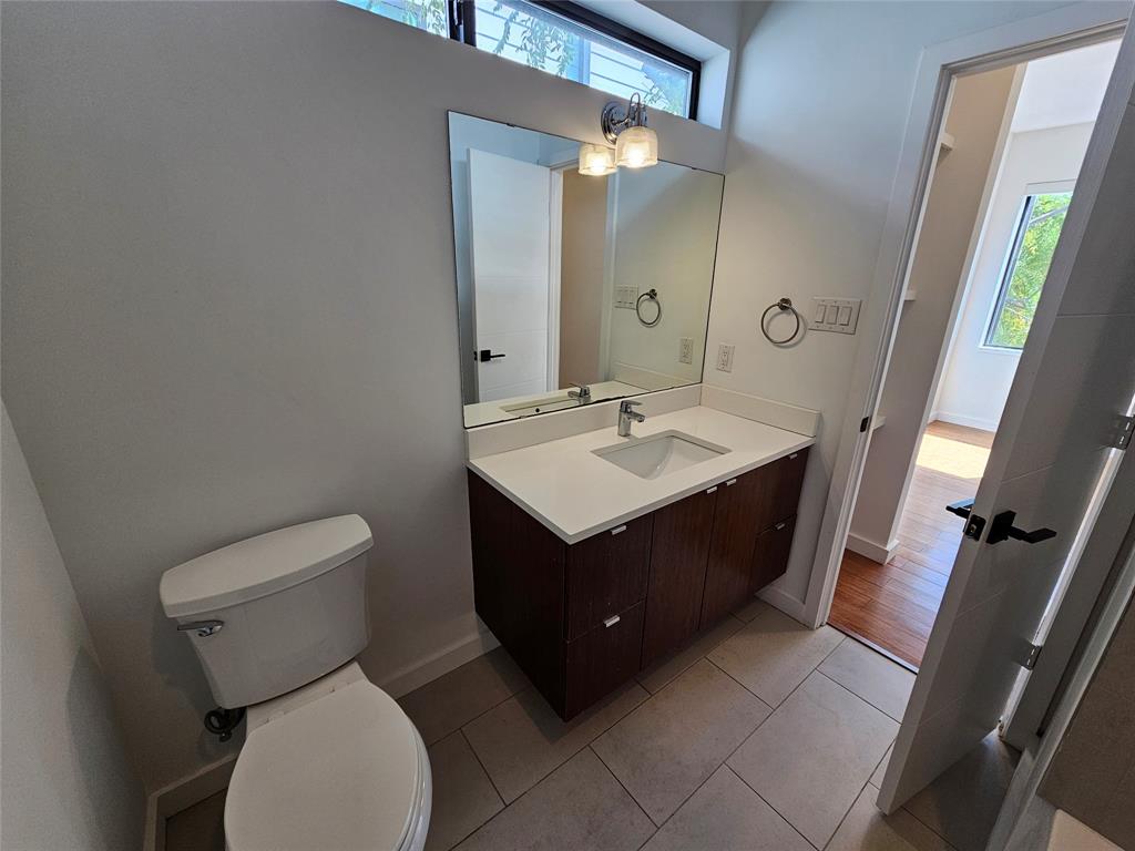 Floating vanity featuring a dark wood-finish cabinet, white solid-surface countertop, rectangular undermount sink, and polished chrome fixtures, complemented by tile flooring and a high-set transom window