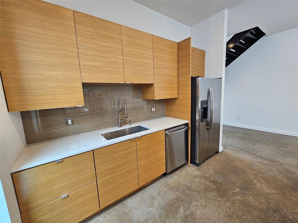 Flat-panel wood-finish cabinetry, white solid-surface countertops, stainless steel appliance suite, tiled backsplash, and polished concrete flooring