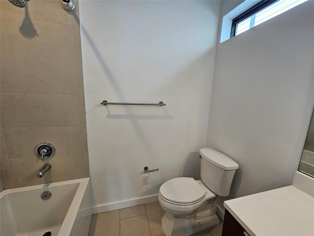 Bathroom featuring a soaking tub with neutral tile surround, a built-in vanity with a solid-surface countertop, high-reach horizontal transom window, and brushed metal fixtures