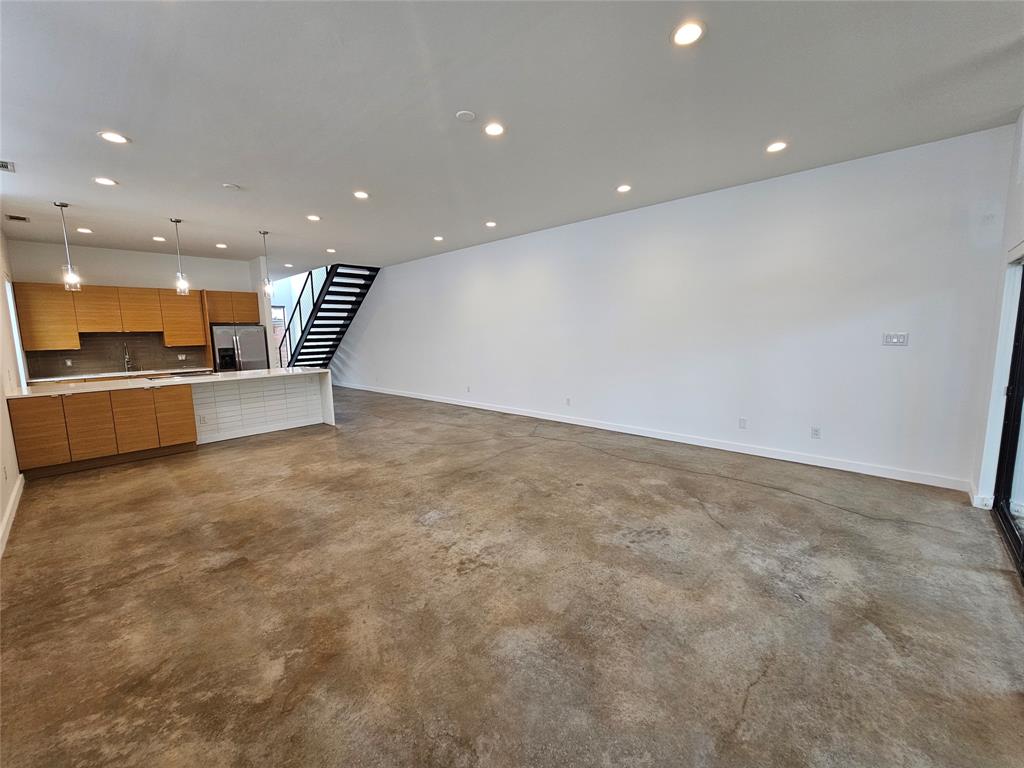 Open floor plan featuring polished concrete flooring, recessed lighting, horizontal wood-grain cabinetry, and a metal floating staircase