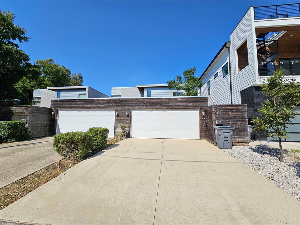 Modern exterior facade featuring horizontal wood siding, two white garage doors, concrete driveway, and a third-level balcony with metal railing