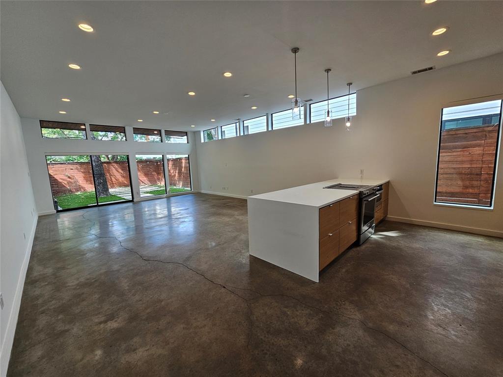 Open-concept living space featuring polished concrete flooring, a kitchen island with stone countertops, wood-finish cabinetry, recessed lighting, and expansive floor-to-ceiling windows