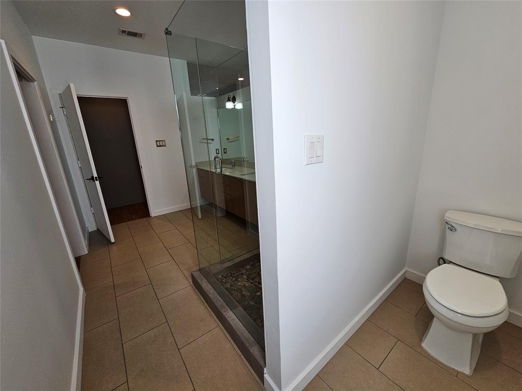 Bathroom featuring large-format tile flooring, a glass-enclosed shower with stone floor inlay, a wood-finish vanity, and recessed lighting