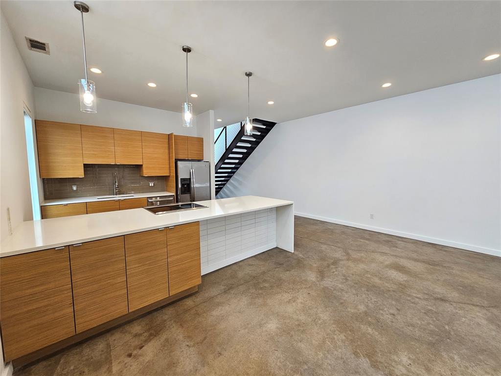 Modern kitchen featuring flat-panel wood-finish cabinetry, a large quartz-topped island with an integrated cooktop, polished concrete flooring, recessed lighting, and glass pendant fixtures