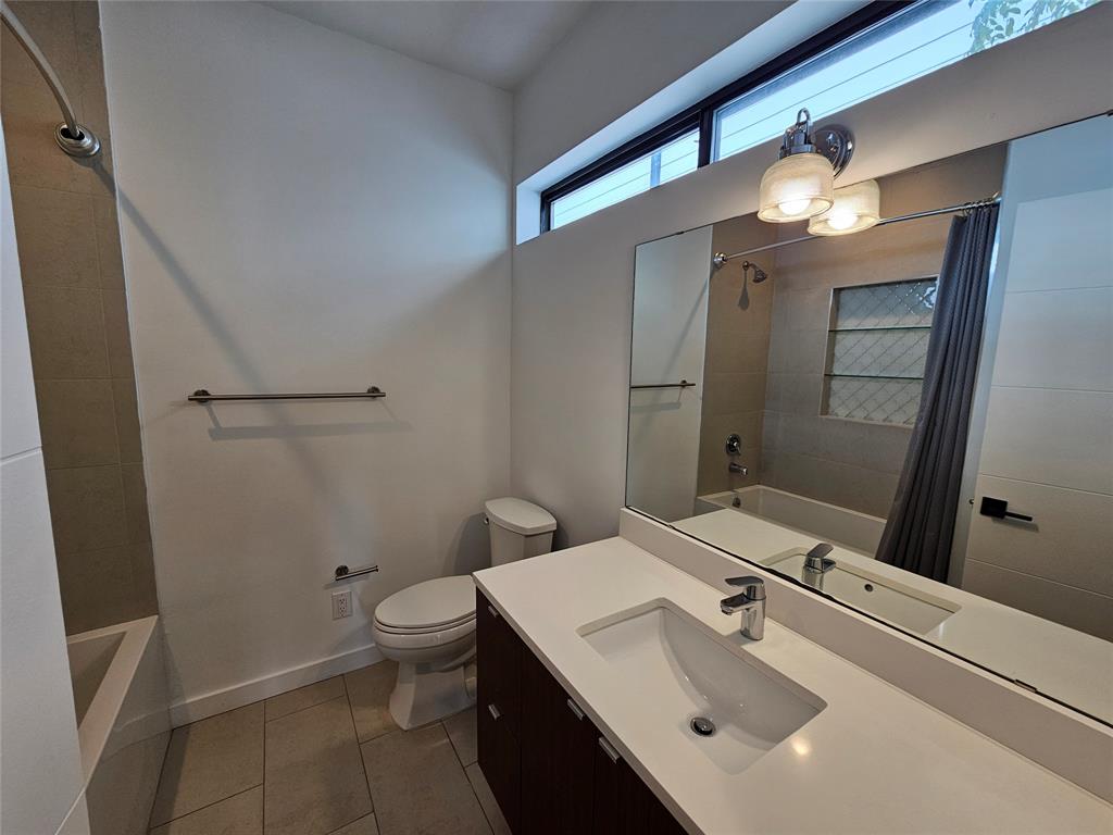 Bathroom featuring a dual-tone vanity with a white countertop, an undermount sink, a large wall-mounted mirror, transom window, and a bathtub with tile surround