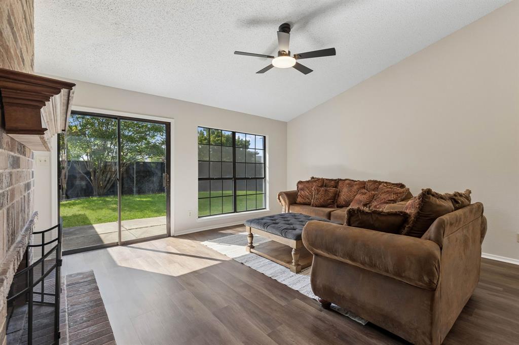 Vaulted ceiling living area featuring a floor-to-ceiling brick fireplace, wood-finish flooring, a multi-blade ceiling fan with integrated lighting, and grid-pane windows