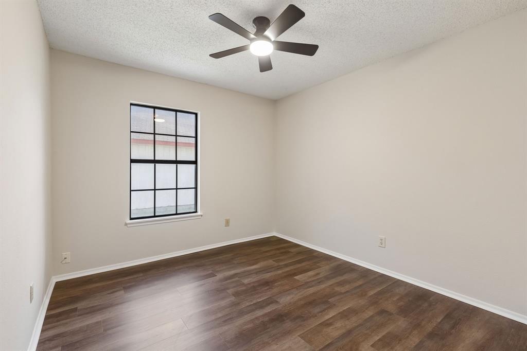 Neutral-toned interior space featuring wood-finish flooring, a multi-pane window with dark trim, and a centralized ceiling fan with integrated lighting