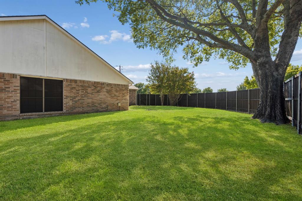 Backyard featuring a manicured lawn, brick and light-toned siding exterior, wood-style perimeter fencing, and a mature tree