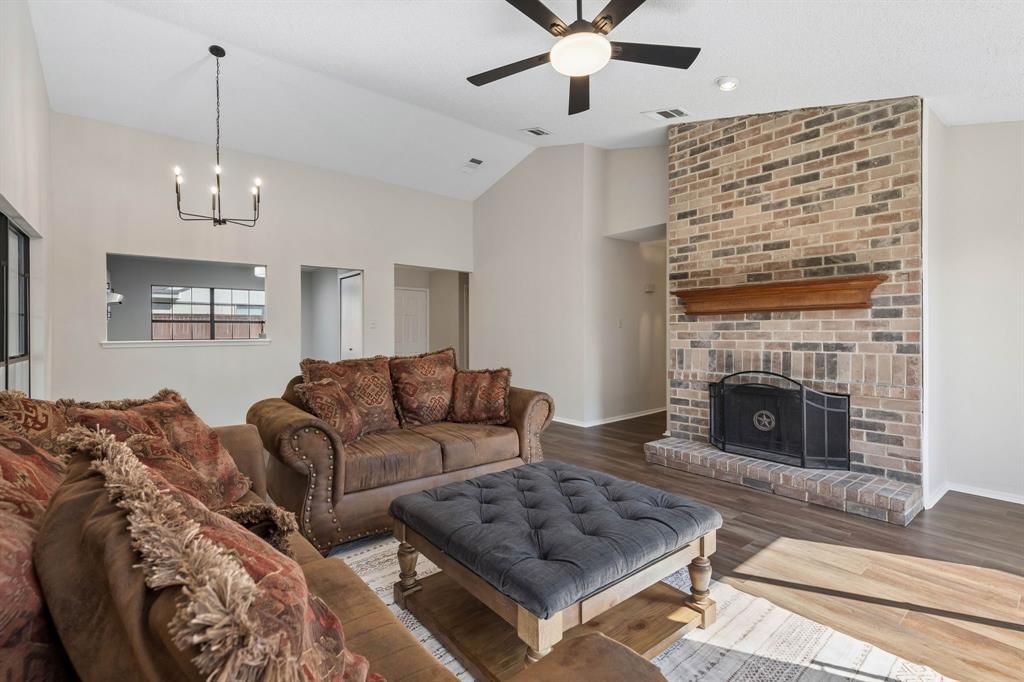 Vaulted ceiling featuring a full-height brick fireplace, wood-finish flooring, a tiered metal chandelier, and a ceiling fan