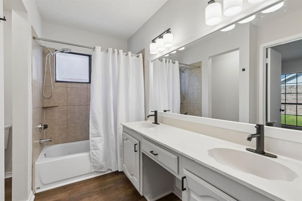 Double vanity featuring a white countertop, dual undermount sinks with matte black faucets, wood-finish flooring, and a full-width wall mirror with integrated lighting
