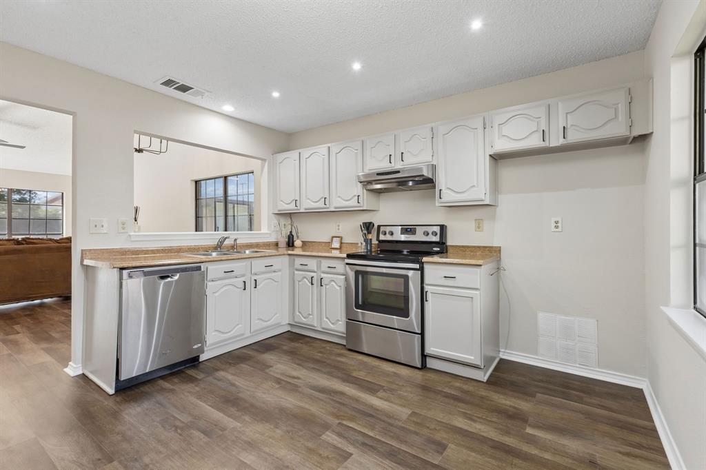 Kitchen featuring wood-finish flooring, white cabinetry, stainless steel appliances, and stone-finish countertops
