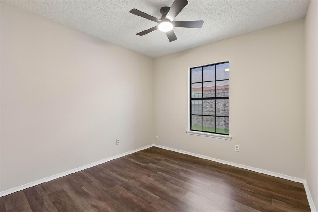 Wood-finish flooring, neutral wall tones, multi-pane window with black frame, and ceiling fan with integrated lighting