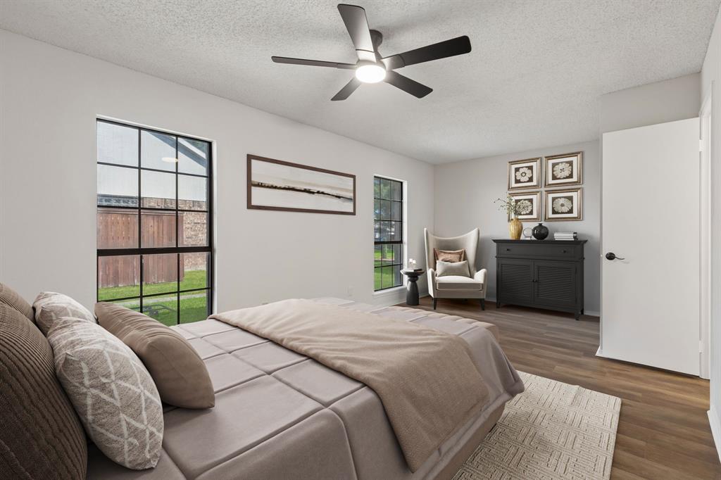 Room featuring wood-finish flooring, dual windows with black frames, and a modern multi-blade ceiling fan with integrated lighting.  Furniture is virtually staged.