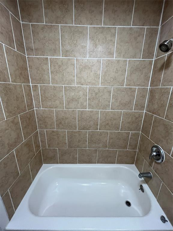 Bathtub surround featuring square, neutral-toned tile with contrasting grout lines, chrome showerhead, and matching chrome faucet assembly