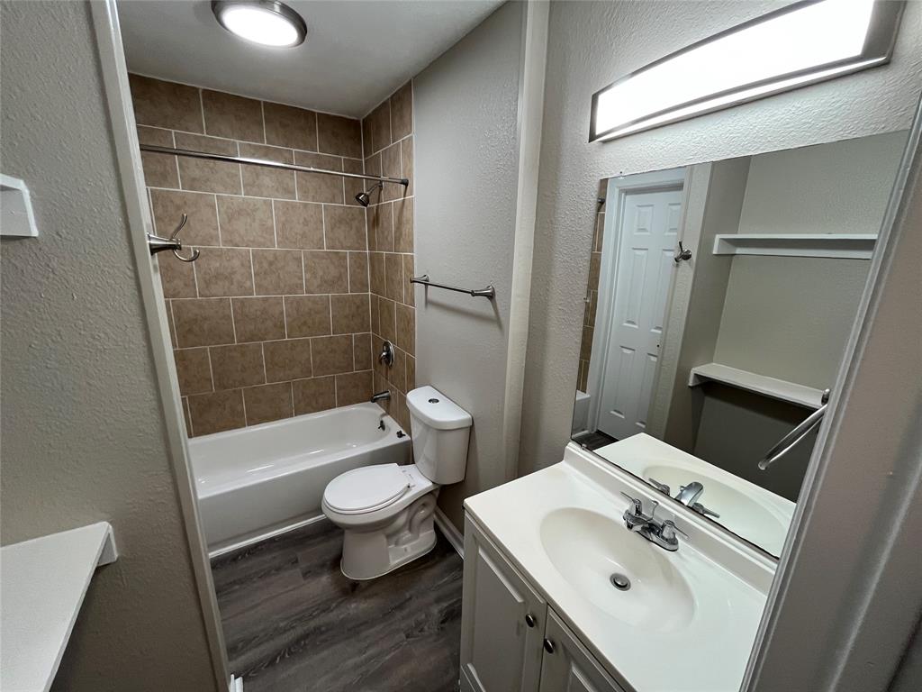 Bathroom featuring wood-finish flooring, vanity with integrated sink, rectangular mirror with integrated lighting, and tile-surround shower and tub combination