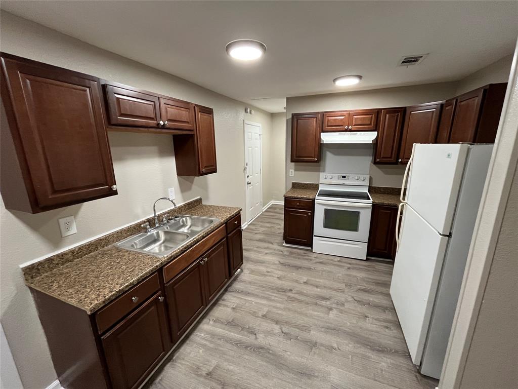 Kitchen featuring dark wood-finish cabinetry, stone-finish laminate countertops, dual-basin stainless steel sink, and wood-finish flooring