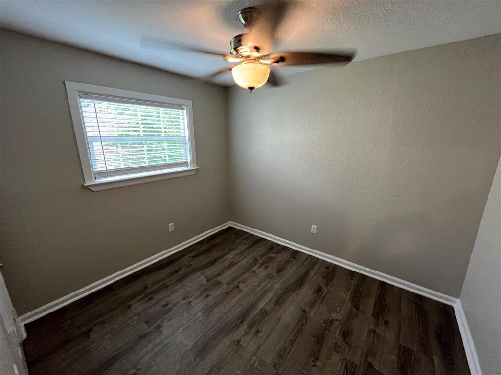 Neutral wall tones, wood-finish flooring, and a central ceiling fan with an integrated light fixture, complemented by a single-pane window with horizontal blinds