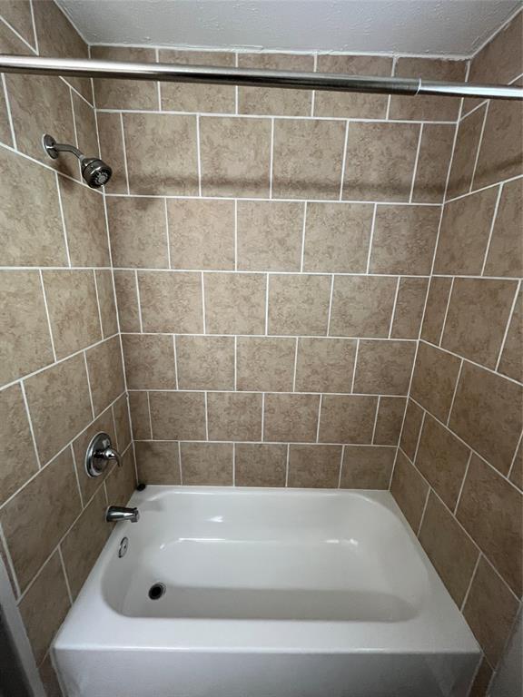 Bathtub featuring a white acrylic finish, full-height tile surround, chrome faucet hardware, and a mounted showerhead