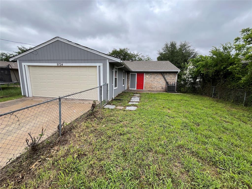 Single-story exterior featuring a grey-painted siding facade, brick masonry accents, a double-car garage, and a chain-link fenced perimeter