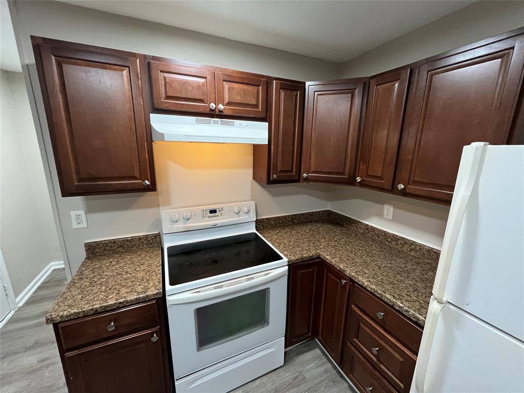 Kitchen featuring dark-toned cabinetry, solid surface countertops, and a white appliance suite including a built-in range hood and electric range
