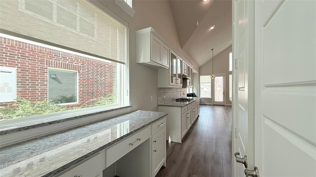 Vaulted ceiling with recessed lighting, stone-surface countertops, custom white cabinetry, and wood-finish flooring Vaulted ceiling with recessed lighting, stone-surface countertops, custom white cabinetry, and wood-finish flooring