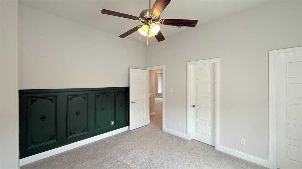 Room featuring wainscoting with decorative paneling, neutral wall coloring, multi-panel doors, carpeting, and a ceiling fan with integrated lighting