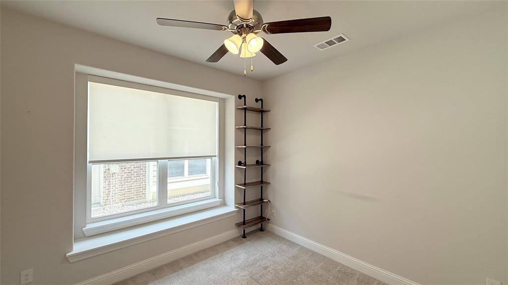 Neutral-toned interior featuring wall-to-wall carpeting, a large window with deep sill, a ceiling fan with integrated light fixture, and floor-to-ceiling industrial-style wall shelving