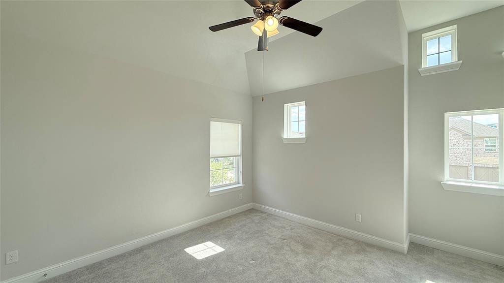 Vaulted ceiling with a central multi-blade ceiling fan, neutral wall tones, carpeted flooring, and multi-pane windows