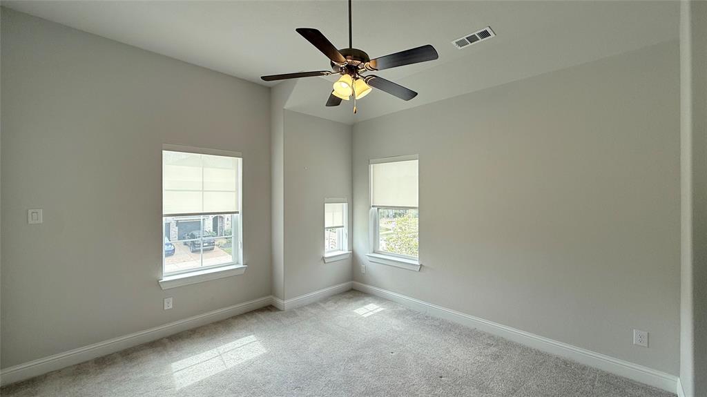 Neutral wall finishes featuring high ceilings, carpeted flooring, and a multi-blade ceiling fan with an integrated light fixture, punctuated by multi-pane windows