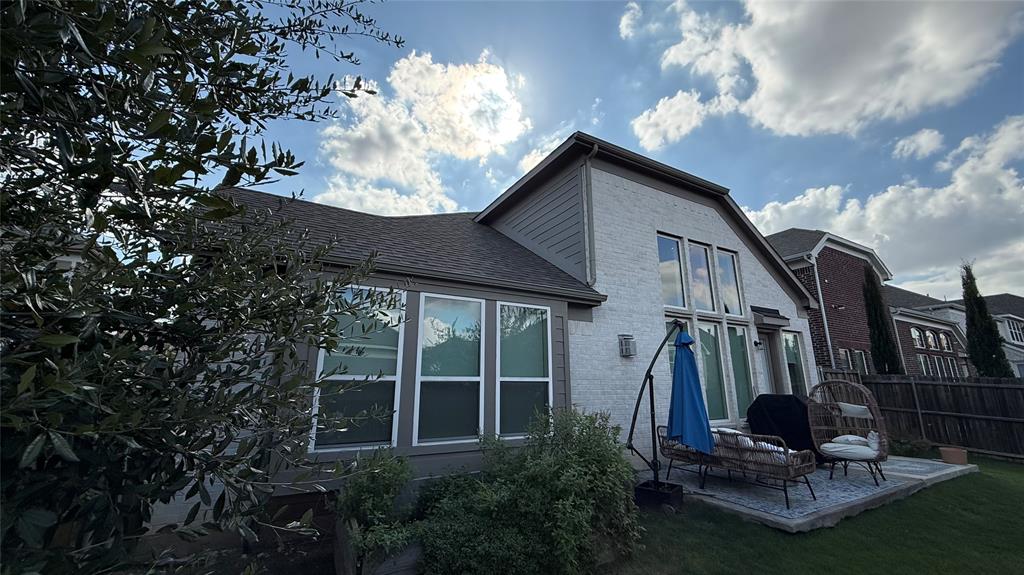 Rear elevation featuring light-toned brick masonry, horizontal siding accents, shingled roofing, and large multi-pane windows