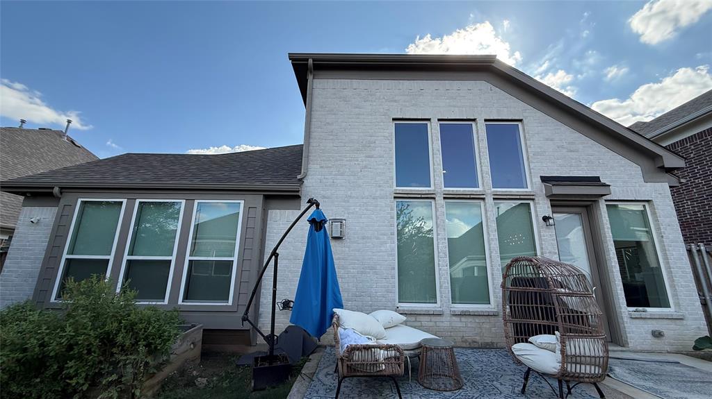 Light-colored brick exterior featuring high-pitched rooflines, expansive vertical windows, and a paved outdoor patio area
