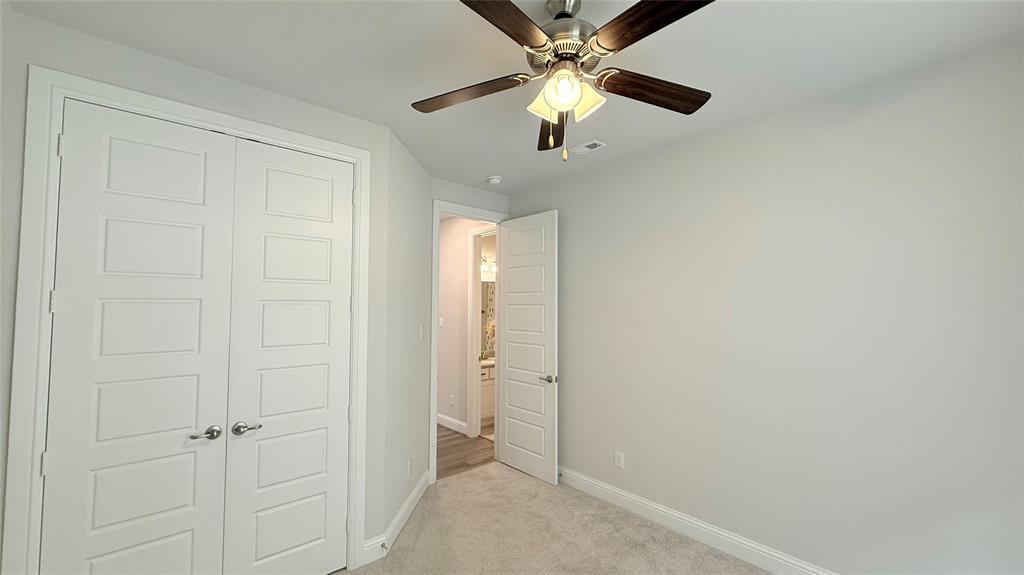 Neutral-toned interior space featuring light-colored wall-to-wall carpeting, five-panel doors, and a brushed nickel ceiling fan with integrated lighting