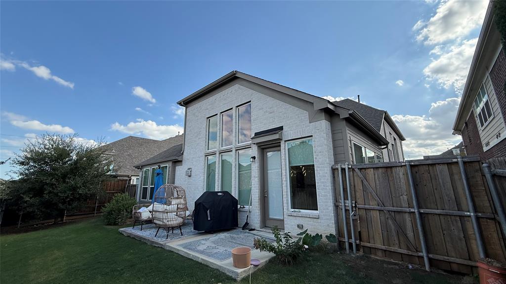 Exterior featuring painted brick siding, vertical windows, a concrete patio, and a wood privacy fence