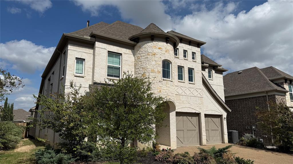 Multi-story residence featuring light-toned brick facade, prominent stone turret, decorative cross-hatching masonry detail, and two-car garage with carriage-style doors Multi-story residence featuring light-toned brick facade, prominent stone turret, decorative cross-hatching masonry detail, and two-car garage with carriage-style doors