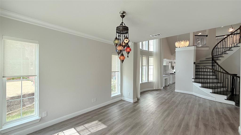 Interior featuring wood-finish flooring, multi-pane windows, a decorative multi-light pendant fixture, and a curved staircase with metal railings