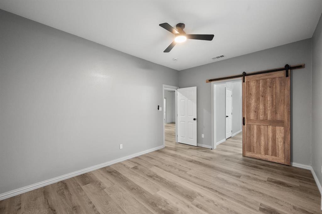 Wood-finish flooring, sliding barn door with black hardware, three-blade ceiling fan with integrated lighting, and traditional six-panel interior doors