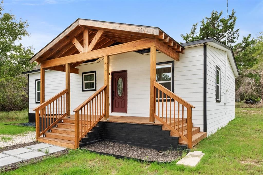Exterior featuring white horizontal siding, a covered front porch with exposed timber beams, wood decking, and a red front door