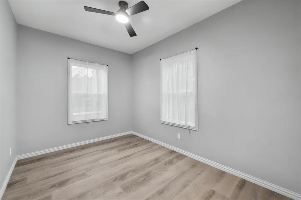 Unfurnished bedroom Neutral-toned walls, wood-finish flooring, two double-hung windows, and a ceiling-mounted light fixture with fan blades